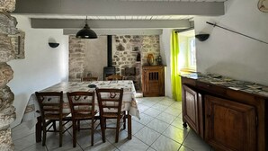 Un comedor rústico con pared de piedra, sillas de madera, una mesa con mantel estampado y una lámpara colgante.