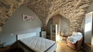 Un dormitorio con techo de piedra, una cama, una mesita de noche, una estantería y una pequeña mesa con lámpara.