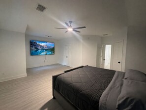 Un dormitorio con cama, ventilador de techo, televisor montado en la pared y una puerta.