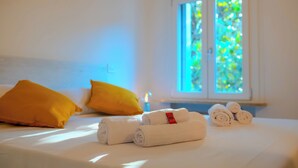 A neatly made bed with rolled towels and a window with a view of greenery. - Segreto Estense: Dormi a un Passo dalla Storia (Ferrara)