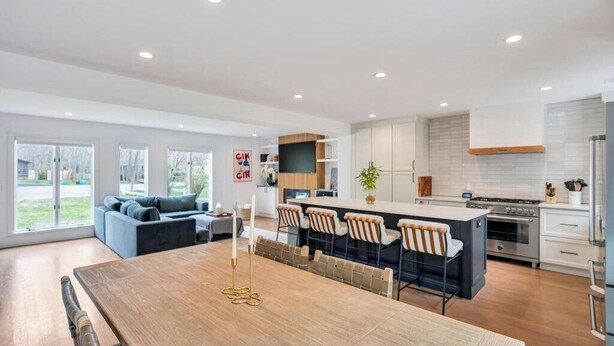 Une cuisine moderne dotée d’un îlot central, un coin repas avec une table en bois et un salon avec un canapé et des fauteuils.