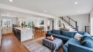 Une cuisine moderne avec un îlot central, un coin repas avec des meubles en bois, un canapé bleu et un escalier.