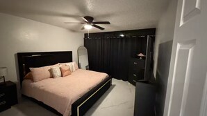 A bedroom with a bed, a ceiling fan, a nightstand, a dresser, and a door.
