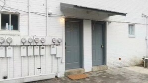 A white building with a grey door, numbered 121, and a row of meters on the wall.