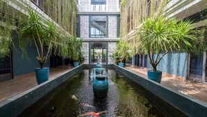 A serene indoor garden with a central water feature, potted plants, and a modern building facade. - Sweet Daisy Retreat (Da Nang)