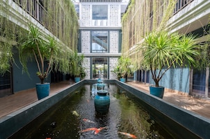 Un jardín interior tranquilo con un elemento central de agua, plantas en macetas y fachada de un edificio moderno.