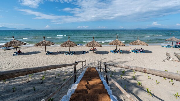 A beach with thatched umbrellas, sun loungers, and a wooden staircase leading to the shore. - Sweet Daisy Retreat (Da Nang)