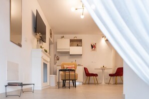 Ein modernes Wohnzimmer mit einer Couch, zwei roten Sesseln, einem kleinen Tisch, einem Flachbildfernseher und einem Kamin.