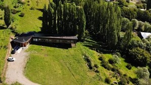 Vista aérea de un edificio con una estructura larga y estrecha, rodeado de campos verdes y árboles exuberantes.