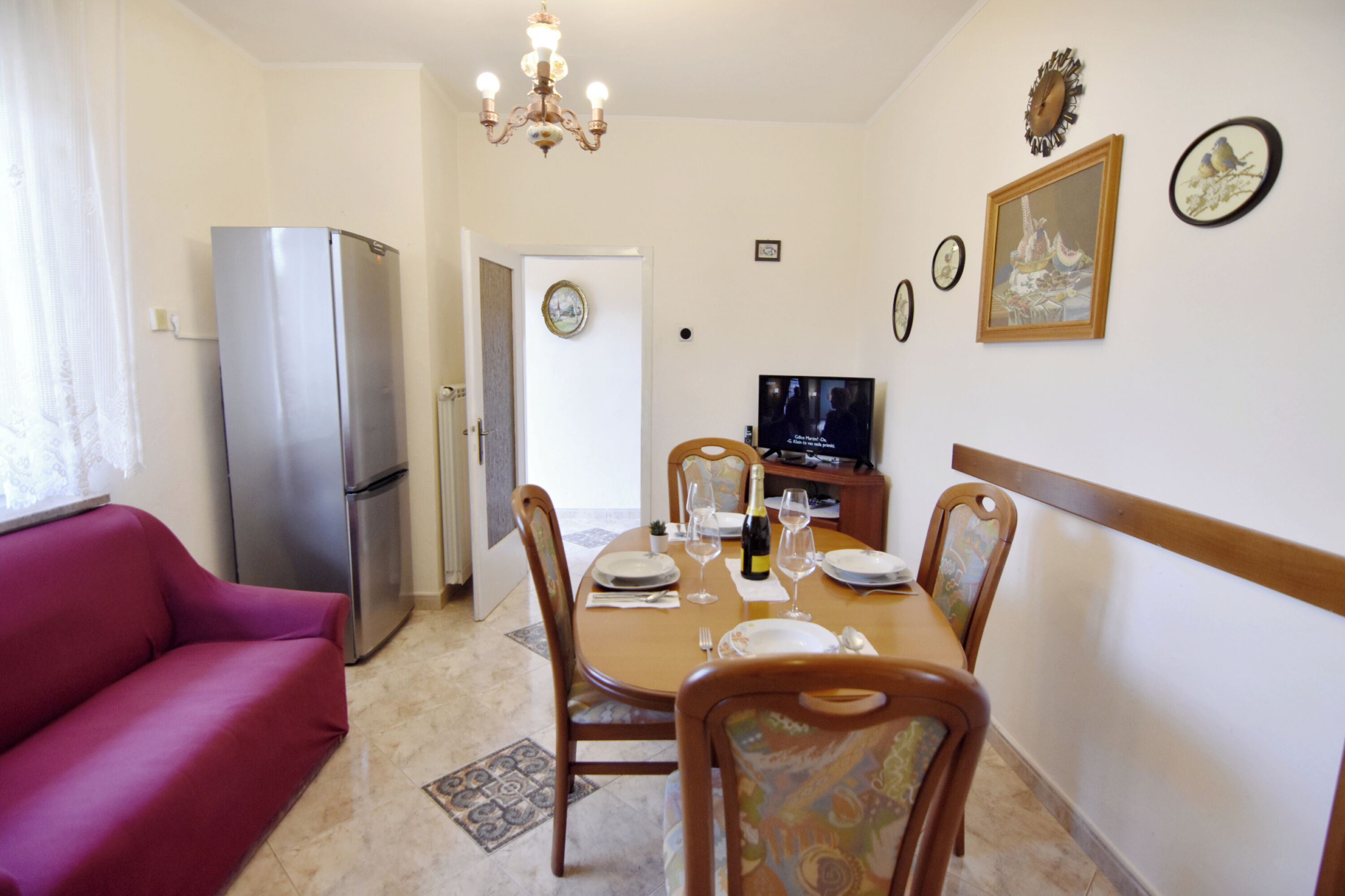 Un coin repas avec une table dressée pour quatre personnes, un canapé, un réfrigérateur et un téléviseur.