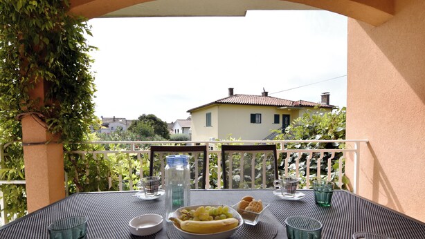 En balkon med et bord dækket til et måltid, inklusive en skål med frugt og glas.