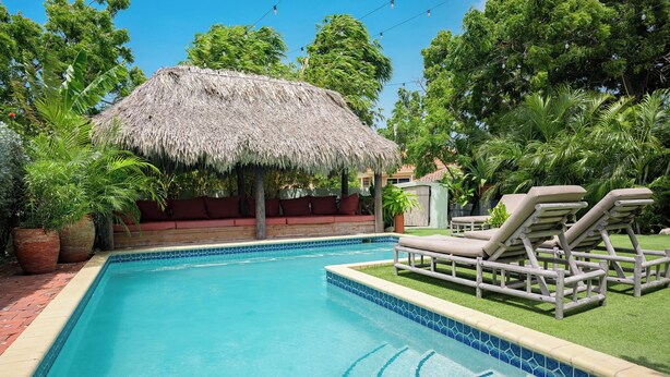 A swimming pool with a thatched roof structure, lounge chairs, and lush greenery. - Happy Hideaway - Private Resort Week, Sleeps 6 (Jan Thiel)