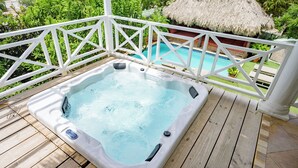Ein Whirlpool auf einer Holzterrasse mit einer überdachten, reetgedeckten Struktur im Hintergrund.