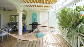 A hammock, a grill, a potted plant, and a wall with a sign. - Happy Hideaway - Private Resort Week, Sleeps 6 (Jan Thiel)