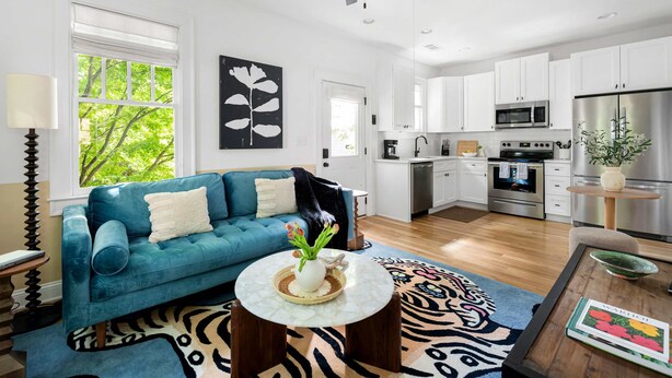 Eine moderne Küche mit weißen Schränken, Edelstahlgeräten und einem Essbereich mit blauem Sofa und gemustertem Teppich.