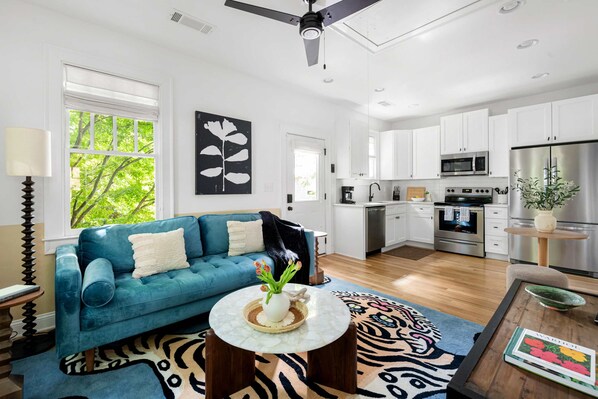 A modern kitchen with white cabinets, stainless steel appliances, and a dining area with a blue sofa and patterned rug.