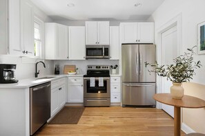 A modern kitchen with white cabinets, stainless steel appliances, a wooden floor, and a small round table with a vase.