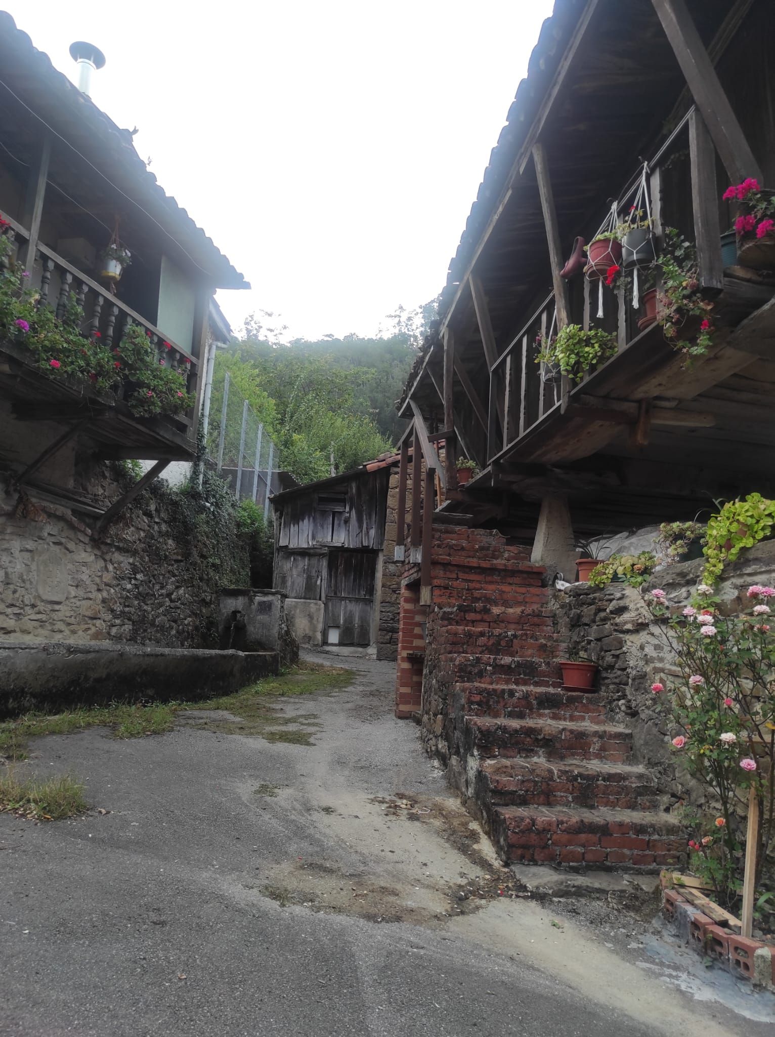 A narrow alleyway with traditional stone buildings, wooden staircases, and hanging flower baskets.