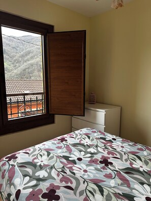 Un dormitorio con cama, ventana, cómoda y una mesita.