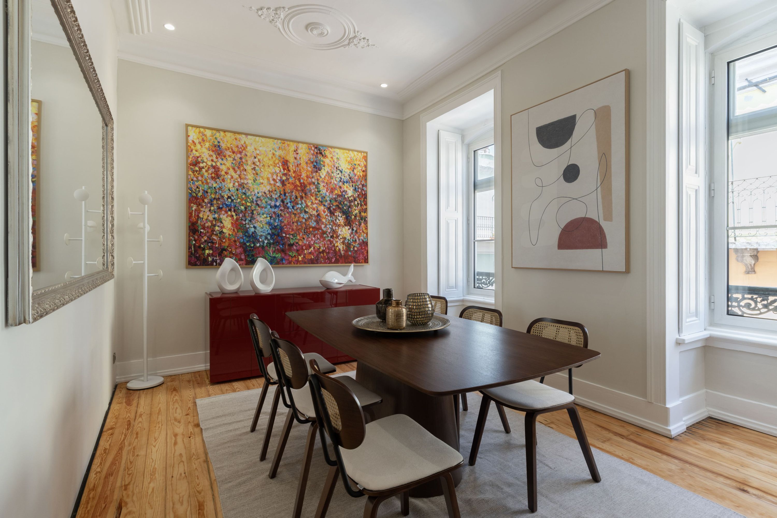 A dining room with a wooden table, chairs, a red cabinet, and two large abstract paintings.