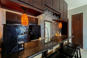 A kitchen with dark wood cabinets, a granite countertop, a black refrigerator, and a hanging light fixture. - Modern 2-Bedroom Oceanview Apartment – Playa Alicia (Sosúa)