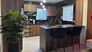 Una cucina moderna con mobili in legno, una parete di fondo in marmo nero e un'isola centrale con sgabelli da bar.