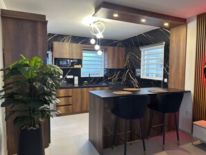 Eine moderne Küche mit Holzschränken, einer schwarzen Marmor-Spritzschutzwand und einer zentralen Kochinsel mit Barhocker.