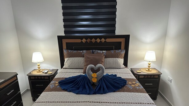 Un letto rifatto con cura, con un'accappatoio a forma di cuore, due comodini con lampade e una testiera con motivo geometrico.