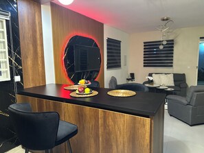 Cocina moderna con una isla central, taburetes de bar y una zona de comedor con sofá y mesa de centro.