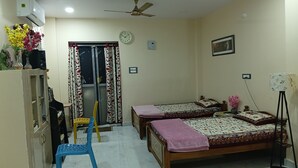 A bedroom with two beds, a desk, a chair, a ceiling fan, and a window with curtains.