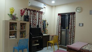 A room with a bookshelf, a desk with a computer, a chair, a bed, and a window with curtains.