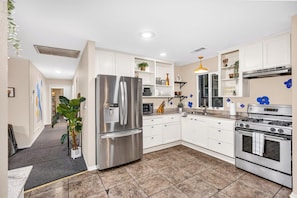 Una cocina moderna con electrodomésticos de acero inoxidable, armarios blancos y piso de baldosas.