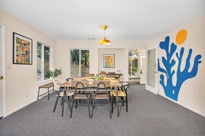 A dining area with a wooden table and chairs, a yellow pendant light, and a large blue wall art piece.