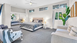 A modern hotel room with a large bed, a sitting area with a chair and a small table, a ceiling fan, and large windows. - Hot Tub-Creekside Yosemite Family Oasis - 5 min to Town-Foosball, Pets Welcome (Mariposa)