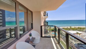 Ein Balkon mit Blick auf Strand und Meer, ein kleiner Tisch mit einer Vase und ein weißer Stuhl.