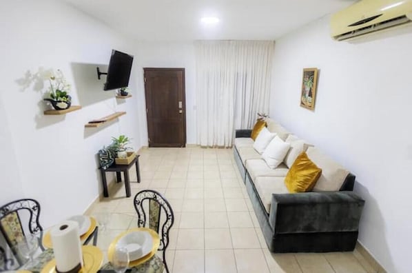Una sala de estar con sofá, televisión y mesa de comedor con sillas.