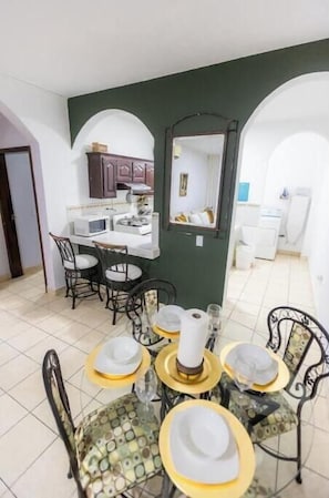 Un comedor con una mesa dispuesta para cuatro personas, un microondas y una cocina al fondo.