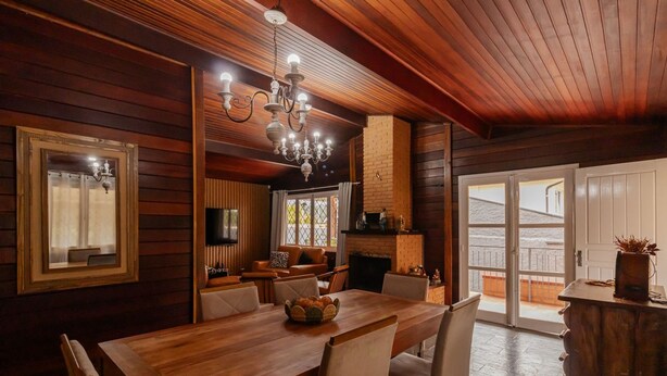 A wooden interior with a dining table, chairs, a chandelier, and a fireplace. - Casa Grande c Lareira e Churrasqueira - Cascatinha (Campos do Jordão)