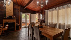 A wooden interior with a fireplace, dining table, chairs, and a chandelier. - Casa Grande c Lareira e Churrasqueira - Cascatinha (Campos do Jordão)