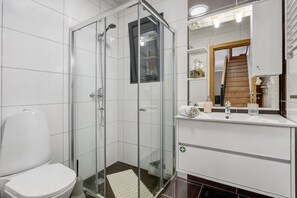A modern bathroom with a glass-enclosed shower, a white toilet, and a vanity with a mirror and sink. - The Cozy Pink House – Ponta do Sol (Canhas)
