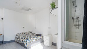 A bedroom with a bed, a bedside table, a small cabinet, and a shower area. - Room 1 - The Archers (Southampton)