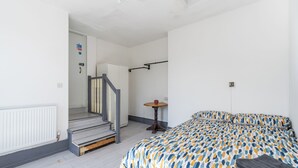 A bedroom with a bed, a small table, a chair, and a staircase leading to another room. - Room 1 - The Archers (Southampton)