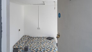 A single bed with a patterned bedspread, a ceiling fan, a wall socket, and a door with a handle. - Room 1 - The Archers (Southampton)