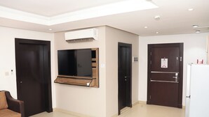 Habitación de hotel moderna con televisión de pantalla plana, aire acondicionado integrado, un mueble de madera y un refrigerador.