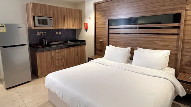 Una habitación de hotel moderna con kitchenette, cama con ropa blanca y una pared de acento de madera.