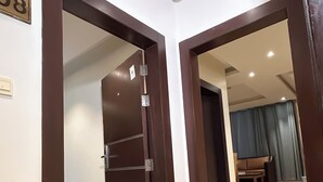 Un pasillo con una puerta, un cartel con el número '08', y una vista parcial de una sala de estar con un sofá y cortinas.