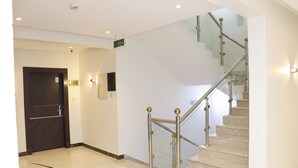 Un vestíbulo de hotel con piso de mármol, una escalera con barandillas de vidrio y una puerta con el número 309.