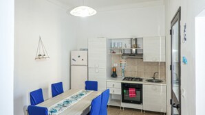 A compact kitchen with a dining area, white cabinetry, a built-in oven, and a hanging light fixture. - Clale House in Marina di Pescoluse (Marina di Pescoluse)