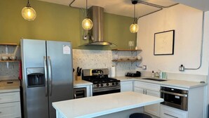Eine moderne Küche mit Edelstahl-Kühlschrank, Gasherd und Backofen, weißen Arbeitsflächen und Barhocker.