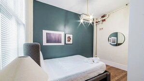 Ein Schlafzimmer mit einem Bett, einer Lampe, einem Deckenventilator, einem an der Wand befestigten Spiegel und gerahmten Bildern.